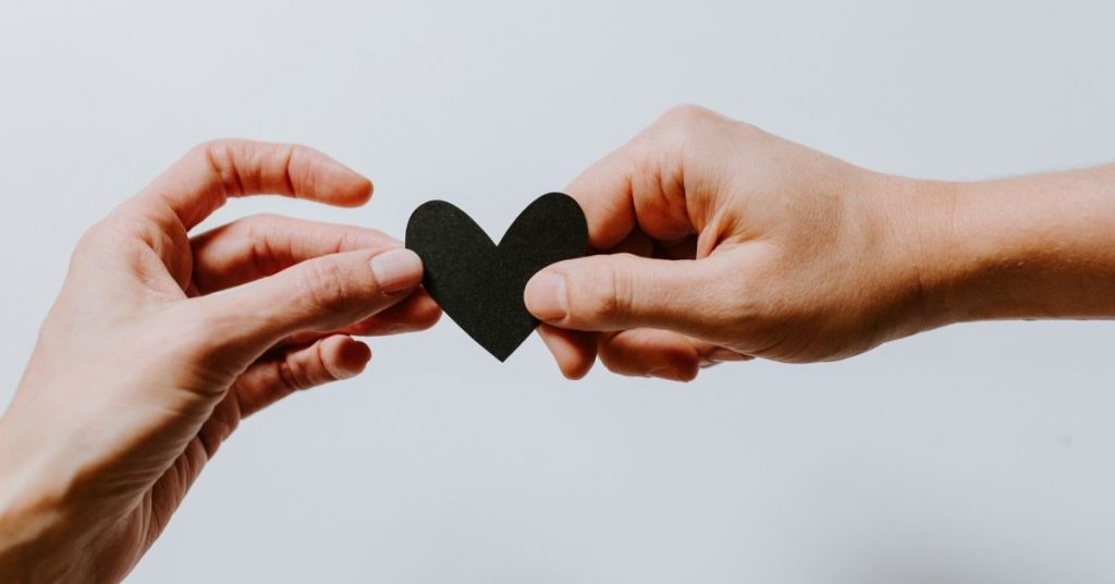 Two hands holding a black heart representing an unhappy relationship on a white background.