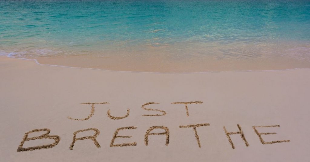 Just breathe written in the sand on a beach.