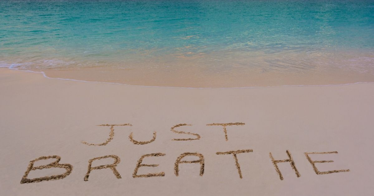 Just breathe written in the sand on a beach.