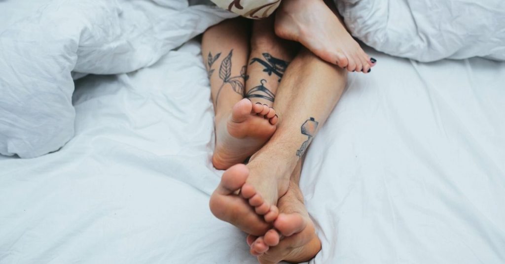 A couple laying on a bed with legs poking through blankets.