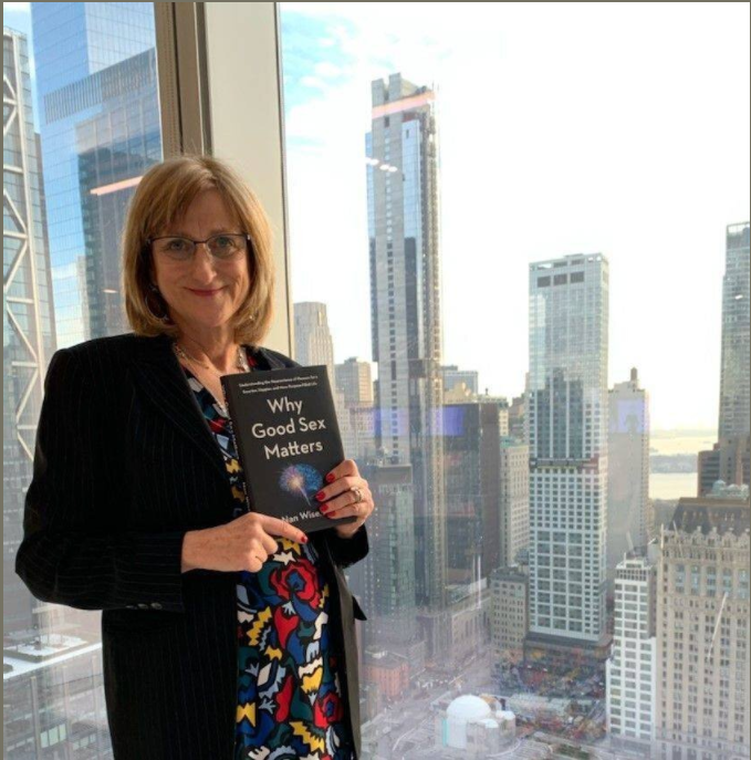 Nan Wise woman holding her book "Why Good Sex Matters" in front of a city skyline.
