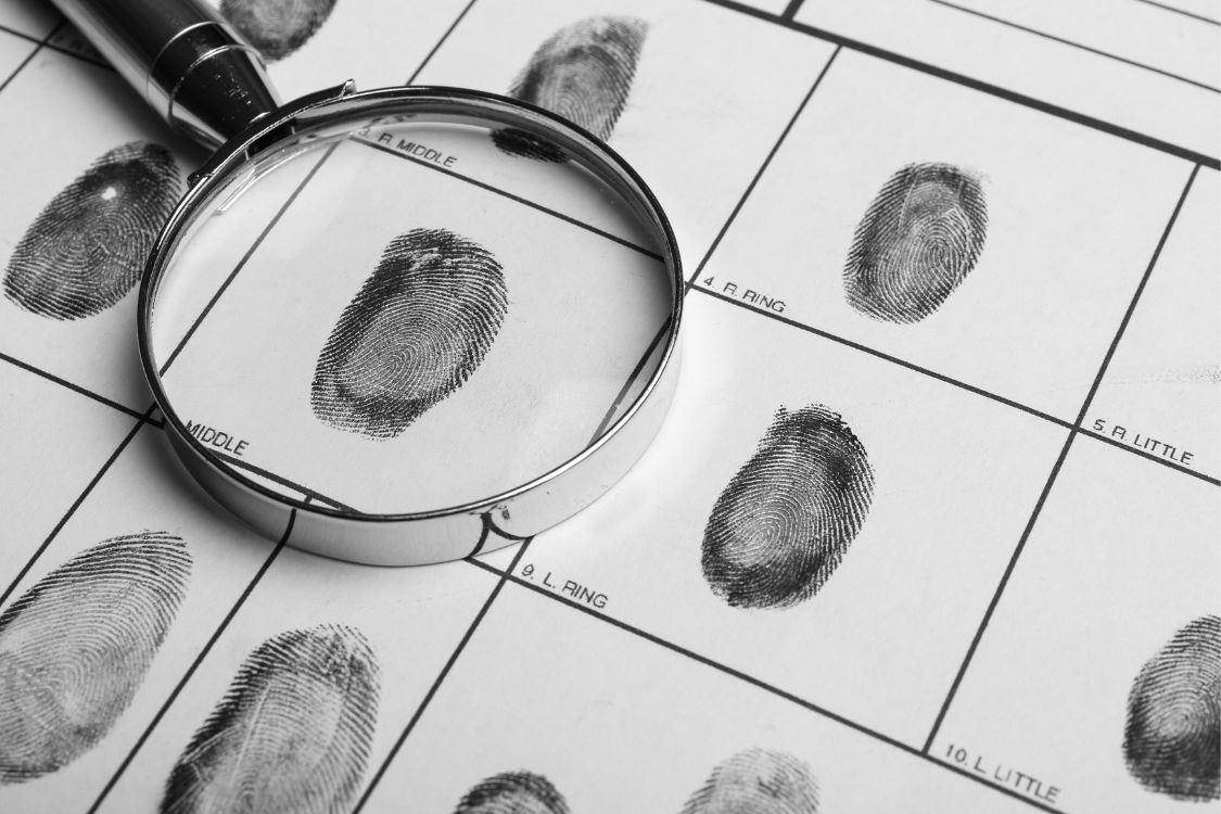 A magnifying glass placed over fingerprint records on a paper sheet, highlighting the prints for closer inspection.
